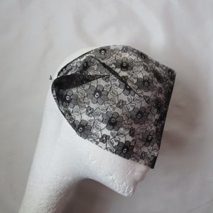 May include: Black lace headband with a floral pattern. The headband is folded in half and is sitting on a white surface.