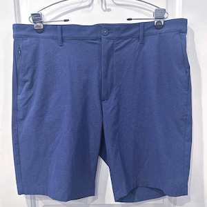 May include: Blue shorts with a textured pattern, featuring a button closure and pockets. The shorts are hanging on a silver hanger. The shorts are a solid blue color.