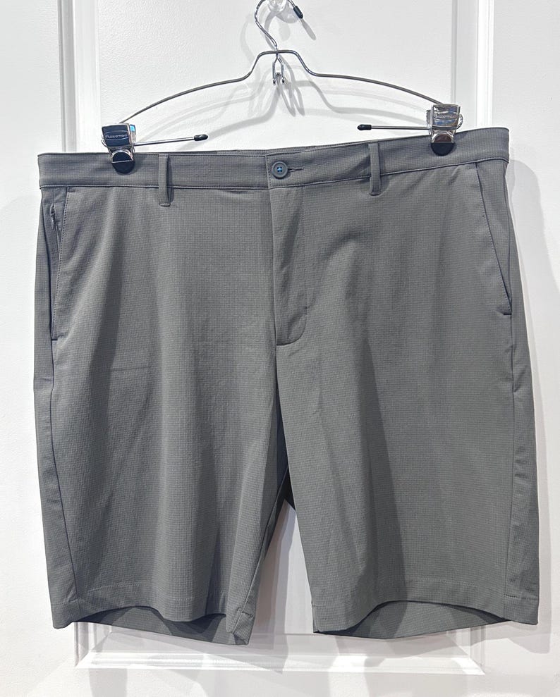 May include: Gray shorts with a button closure, belt loops, and side pockets. The shorts are hanging on a metal hanger against a white background. The fabric has a subtle textured pattern.