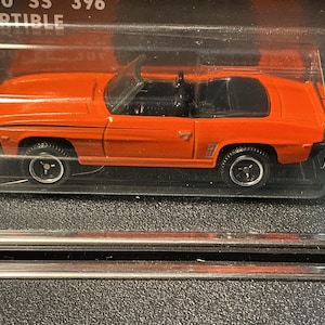 May include: Orange die-cast model of a Camaro SS 396 convertible. The toy car is in a clear plastic package. The car has black tires and a black interior. The model is a 1/6 scale.
