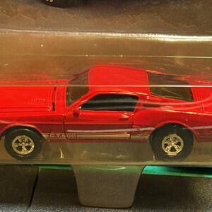 May include: A bright red die-cast toy car model of a Ford Mustang Shelby G.T.500, featuring gold-colored wheels and gold side-stripe detailing with the text G.T.500, enclosed in its original clear plastic blister packaging for protection.