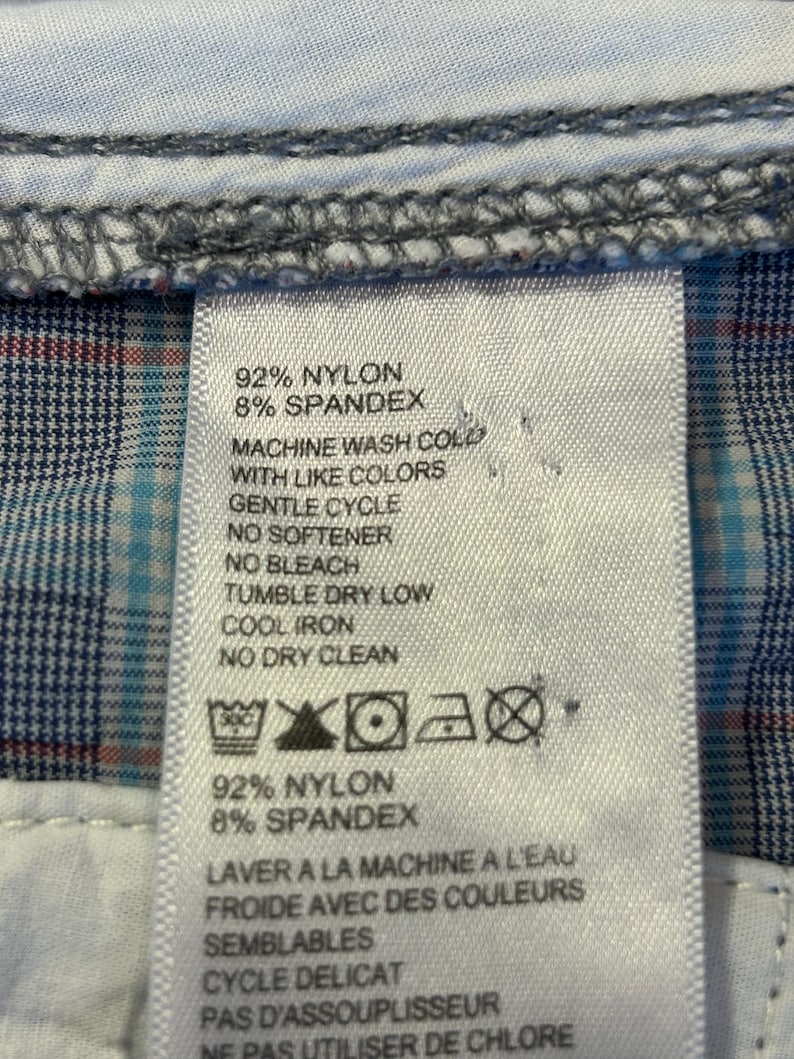 May include: Close-up of a clothing tag with care instructions. The tag lists the fabric composition as 92% nylon and 8% spandex. Washing instructions include machine wash cold with like colors, gentle cycle, no softener, no bleach, tumble dry low, cool iron, and no dry clean.