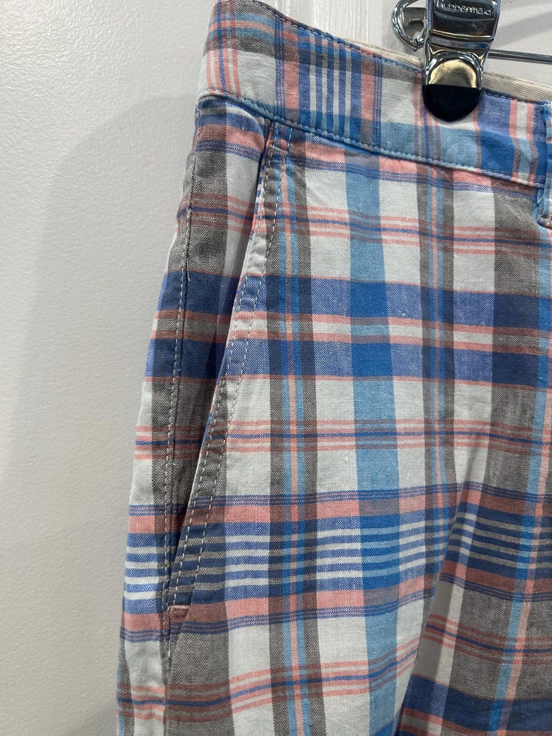 Peut inclure: Gros plan sur un short &agrave; carreaux bleu, blanc, rose et gris. Le short a une poche avant et une fermeture boutonn&eacute;e. Le tissu a une texture tiss&eacute;e.