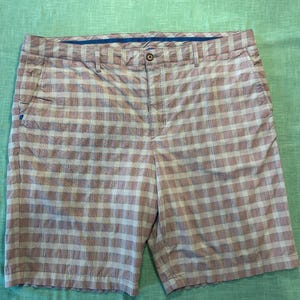 May include: Brown and white plaid shorts with a button closure and belt loops. The shorts have two front pockets and two back pockets. The shorts are made of a lightweight material and are suitable for casual wear.