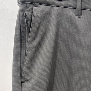May include: Close-up of gray pants with a textured, grid-like pattern. The pants have a zippered pocket on the side and a belt loop. The fabric appears to be a lightweight, breathable material, suitable for warm weather.