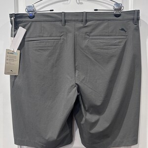 May include: Gray golf shorts with a textured pattern, featuring back pockets and belt loops. A tag with the brand name "ISLAND" is attached. The shorts are hanging on a metal hanger.