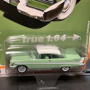 May include: A mint green and white 1958 Plymouth Belvedere diecast model car. The model is 1:64 scale and features chrome accents, white wall tires, and the text "true 1:64". The car is in a clear plastic package.