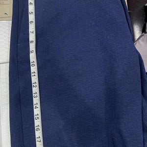 May include: Navy blue shorts with a textured pattern. The shorts are measured with a ruler, showing a length of approximately 20 inches. The shorts have a button and a zipper closure.