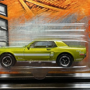 May include: A lime green 1968 Ford Mustang GT/CS die-cast toy car with a white side stripe, black wheels, and silver trim, encased in its original clear plastic blister packaging with the text 1968 FORD MUSTANG GT/CS printed on the side.
