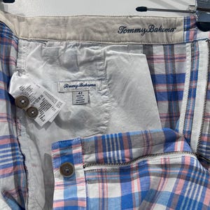 Peut inclure: Gros plan d'un short &agrave; carreaux Tommy Bahama bleu, rose et blanc. Le short a une fermeture &eacute;clair, une fermeture &agrave; bouton et une &eacute;tiquette indiquant "Tommy Bahama". Le short est suspendu &agrave; un cintre.