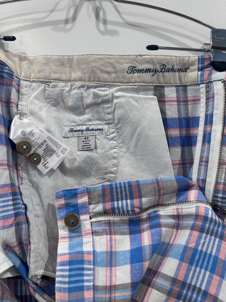 Peut inclure: Gros plan d'un short &agrave; carreaux Tommy Bahama bleu, rose et blanc. Le short a une fermeture &eacute;clair, une fermeture &agrave; bouton et une &eacute;tiquette indiquant "Tommy Bahama". Le short est suspendu &agrave; un cintre.