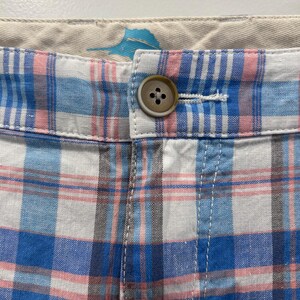 Peut inclure: Gros plan sur un short &agrave; carreaux bleu, rose et blanc. Un bouton marron ferme la ceinture. Le tissu semble l&eacute;ger. Le motif &agrave; carreaux est un motif classique.