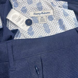 May include: Close-up of navy blue dress pants with a textured pattern. The interior lining features a white fabric with a blue pineapple design. A label reads "Tommy Bahama" and "40".