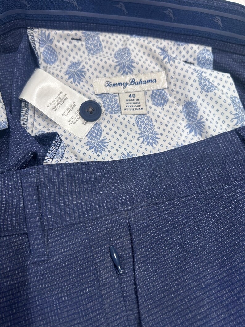 May include: Close-up of navy blue dress pants with a textured pattern. The interior lining features a white fabric with a blue pineapple design. A label reads "Tommy Bahama" and "40".
