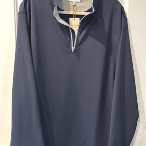 May include: Navy blue long-sleeve pullover with a quarter-zip closure and a stand-up collar. The shirt has a tag attached with the brand name "PETER MILLAR". The garment is hanging on a pink hanger.