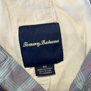 May include: Close-up of a navy blue Tommy Bahama label, size 40, sewn into the lining of a plaid garment. The label indicates the garment is made in China of 92% nylon and 8% spandex. The plaid pattern includes blue, red, and white.
