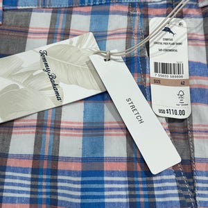 Peut inclure: Gros plan d'un short &agrave; carreaux bleu, rose, blanc et gris. Le short porte une &eacute;tiquette avec les mentions "Tommy Bahama" et "STRETCH". La taille est 42.