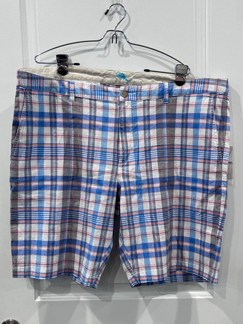 Peut inclure: Short short en tissu &agrave; carreaux bleus, blancs et roses, suspendu &agrave; un cintre en m&eacute;tal. Le short est dot&eacute; d'une fermeture boutonn&eacute;e et de poches. Le motif &agrave; carreaux est un design classique, adapt&eacute; au quotidien.