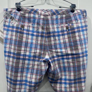 Peut inclure: Shorts &agrave; carreaux bleus, blancs, roses et gris suspendus &agrave; un cintre en m&eacute;tal. Les shorts ont deux poches arri&egrave;re avec des fermetures &agrave; boutons et une fermeture &agrave; bouton et fermeture &eacute;clair &agrave; l'avant. Une &eacute;tiquette est attach&eacute;e.