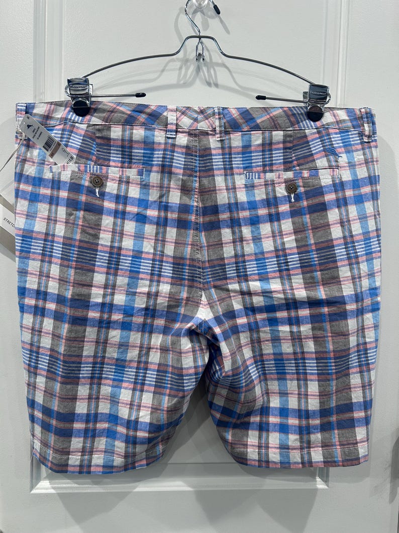 Peut inclure: Shorts &agrave; carreaux bleus, blancs, roses et gris suspendus &agrave; un cintre en m&eacute;tal. Les shorts ont deux poches arri&egrave;re avec des fermetures &agrave; boutons et une fermeture &agrave; bouton et fermeture &eacute;clair &agrave; l'avant. Une &eacute;tiquette est attach&eacute;e.