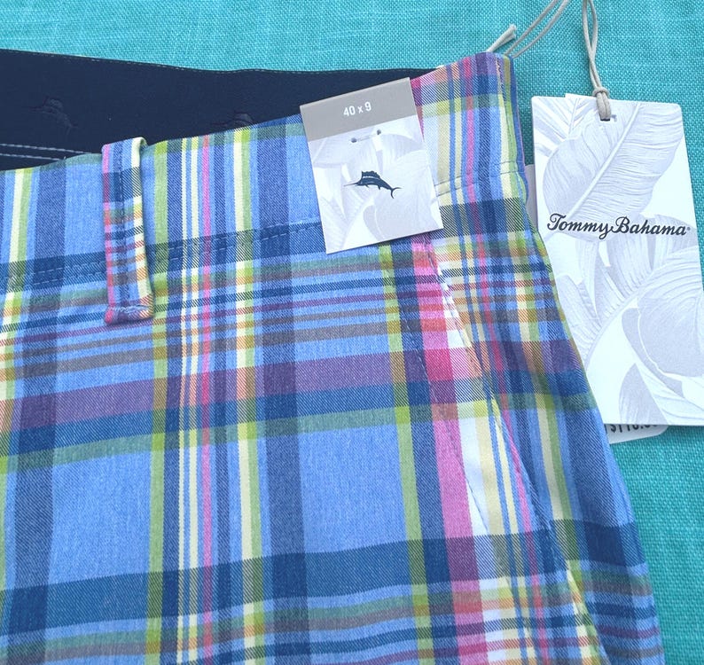 K&ouml;nnte beinhalten: Nahaufnahme von karierten Shorts in Blau, Rosa, Gelb und Wei&szlig;. Die Shorts haben ein Etikett mit der Aufschrift "Tommy Bahama" und ein weiteres Etikett mit den Ma&szlig;en "40 x 9" und einem Logo. Die Shorts sind aus leichtem Stoff.