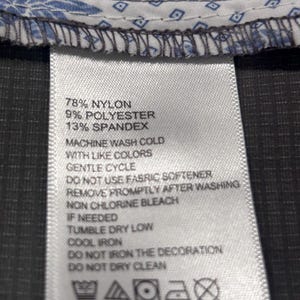 May include: Close-up of a clothing label with care instructions. The label lists the fabric composition as 78% nylon, 9% polyester, and 13% spandex. Washing instructions include machine wash cold, gentle cycle, and tumble dry low.