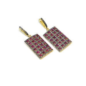 May include: A pair of rectangular earrings with a gold-colored frame. The earrings are encrusted with small, square, ruby-red stones and tiny, silver-colored stones. The earrings have a gold-colored hook closure.