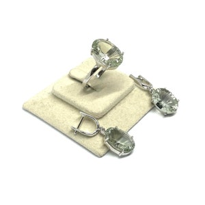 May include: A set of silver earrings and a ring with green gemstone accents. The earrings are dangle style with a teardrop shaped stone. The ring has a large oval shaped stone.