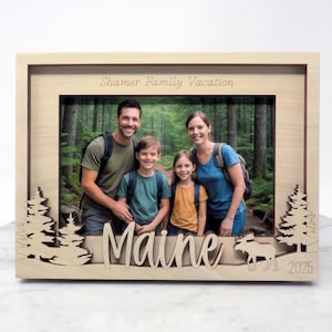 May include: A wooden photo frame with a family portrait. The frame has laser-cut pine trees and the word "Maine" in script. An image of a moose and the year 2025 are also included. The text "Shamer Family Vacation" is engraved at the top.
