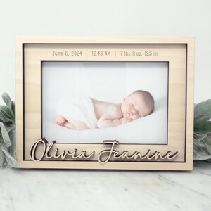 May include: A wooden photo frame with a light wood finish. The frame has a cutout for a photo and a personalized inscription that reads "June 5, 2024 | 12:43 AM | 7 lbs 8 oz. 195 in" and "Olivia Jeanine".
