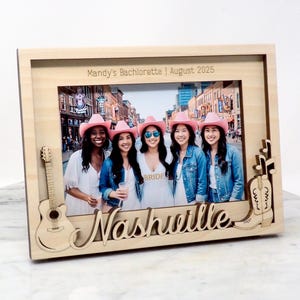 May include: Wooden photo frame with a picture of five women wearing pink cowboy hats. The frame has a guitar and boot design, with the word "Nashville" and the text "Mandy's Bachelorette 1 August 2025".