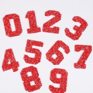May include: Ten red sparkly iron-on numbers, 0 through 9, for decorating clothing or crafts.