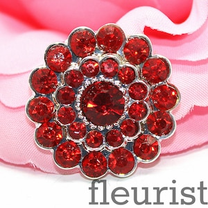 May include: A red rhinestone flower embellishment with a silver metal setting. The flower is made up of many small red rhinestones arranged in a circular pattern.