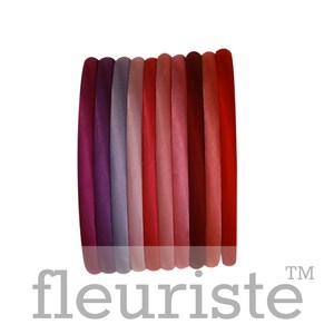 May include: A set of ten hair elastics in various shades of red, pink, and purple. The elastics are arranged in a stack, with the darkest shade at the bottom and the lightest shade at the top.