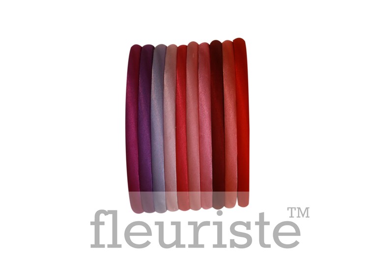 May include: A set of ten hair elastics in various shades of red, pink, and purple. The elastics are arranged in a stack, with the darkest shade at the bottom and the lightest shade at the top.