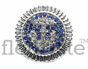 Puede incluir: Broche plateada con un diseño de ancla de cristal azul y blanco. El ancla está rodeada por un círculo de cristales azules. La broche tiene un borde circular texturizado.