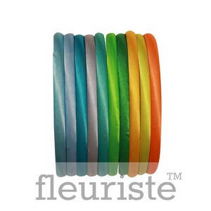 May include: A set of ten colorful satin headbands in shades of blue, green, yellow, and orange. The headbands are arranged in a stack, with the colors transitioning from light to dark.