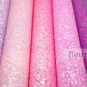 May include: Five rolls of glitter fabric in shades of purple, pink, and white. The fabric is textured and has a sparkly finish.