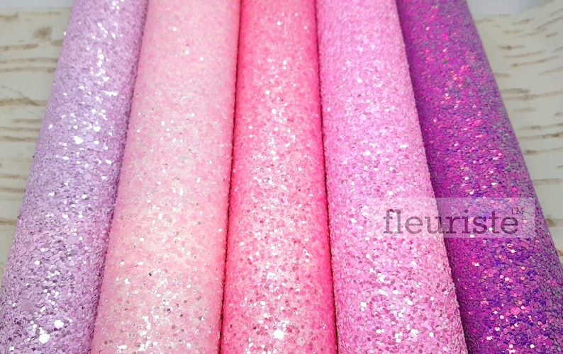 May include: Five rolls of glitter fabric in shades of purple, pink, and white. The fabric is textured and has a sparkly finish.