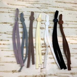 K&ouml;nnte beinhalten: Sortiment von acht elastischen Schnurextendern f&uuml;r Masken mit verschiedenen farbigen Schn&uuml;ren und Plastikstopfen. Die Schn&uuml;re sind in den Farben Braun, Grau, Beige, Wei&szlig;, Schwarz und Lila.