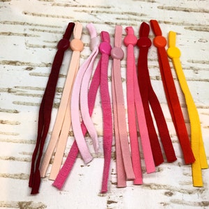 K&ouml;nnte beinhalten: Sortiment an bunten elastischen Maskenverl&auml;ngerungen mit Plastikkn&ouml;pfen. Die Verl&auml;ngerungen sind in Rot-, Rosa-, Orange- und Gelbt&ouml;nen.