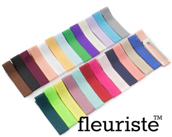 May include: Assortment of 20 colorful ribbon hair clips with a silver alligator clip. The ribbons are in various colors, including red, pink, blue, green, yellow, and brown. The clips are arranged in a fan shape on a white background. The text "fleuriste" is printed in black at the bottom of the image.