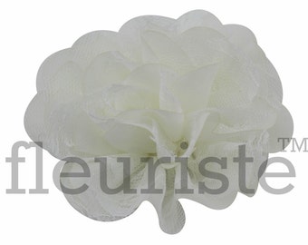May include: A white, fabric flower with a ruffled texture. The flower is made of a delicate, sheer material and has a soft, romantic look. The flower is labeled "fleuriste" with a trademark symbol.