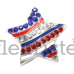 May include: A silver star-shaped pin with red, white, and blue stripes and rhinestones. The star is decorated with blue, red, and clear rhinestones.