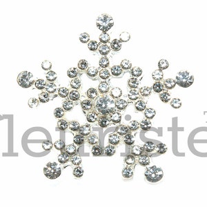 May include: A silver snowflake ornament with clear rhinestones. The snowflake is a popular Christmas decoration.