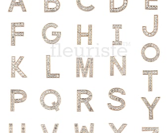 Puede incluir: Encantos de letras del alfabeto en tono dorado con adornos de cristal transparente. Cada letra se muestra individualmente sobre un fondo blanco.