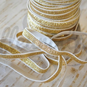 May include: White elastic ribbon with a gold glitter trim. The ribbon is rolled up and there are several loops of the ribbon.