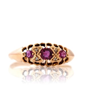 May include: A gold ring with three ruby stones and two diamond accents. The ring has a delicate, intricate design.