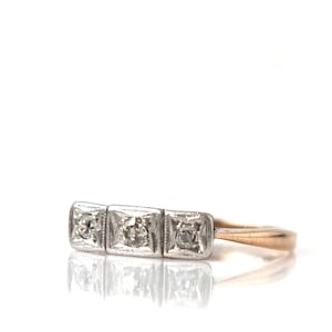 May include: A vintage three-stone diamond ring with a gold band. The center stone is surrounded by two smaller stones, all set in a white metal.