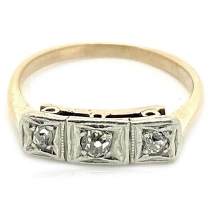 May include: A gold band ring with three square-shaped settings, each containing a small round diamond. The ring is made of both yellow and white gold.